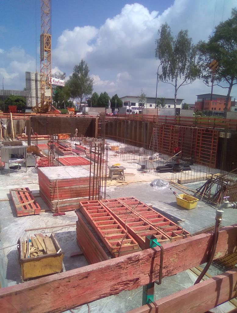 Budowa fundamentów budynku, widoczne szalunki, zbrojenia, dźwig w tle i budynek Kaufland, etap prac ziemnych.