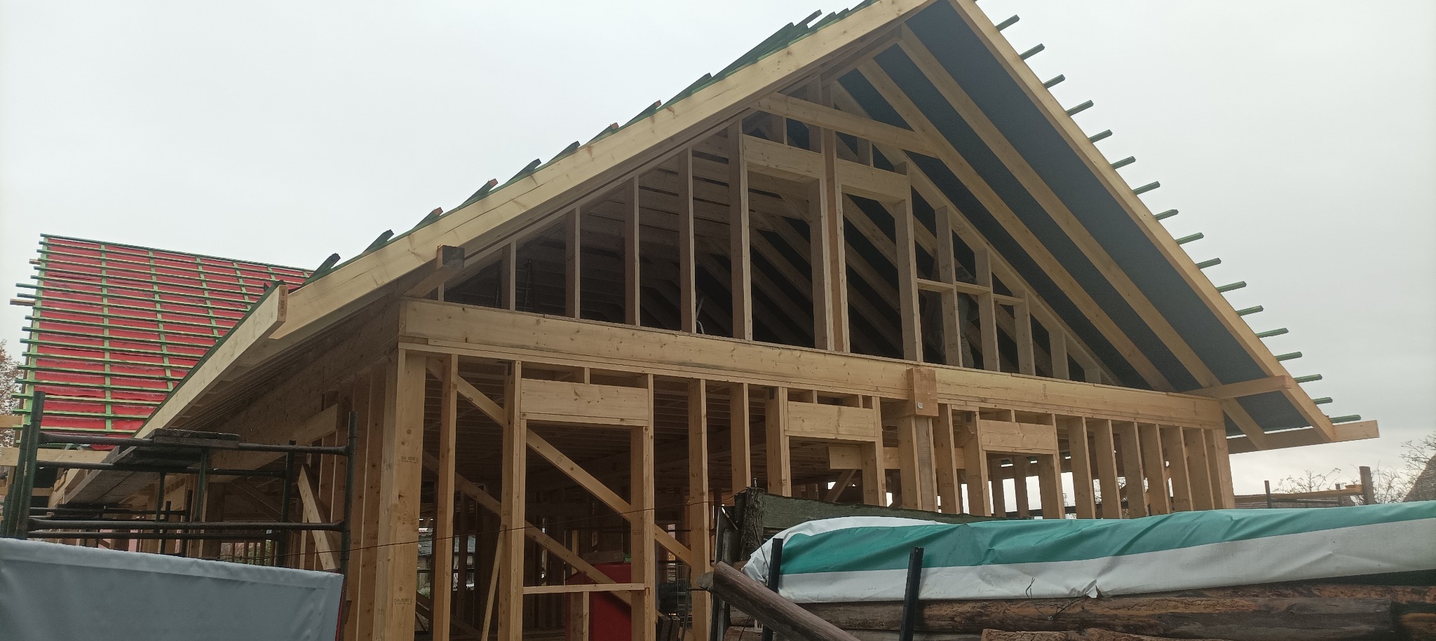 Konstrukcja domu w trakcie budowy: drewniany szkielet z widoczną więźbą dachową i częściowo pokrytym dachem. Ujęcie z dołu, pochmurne niebo w tle.