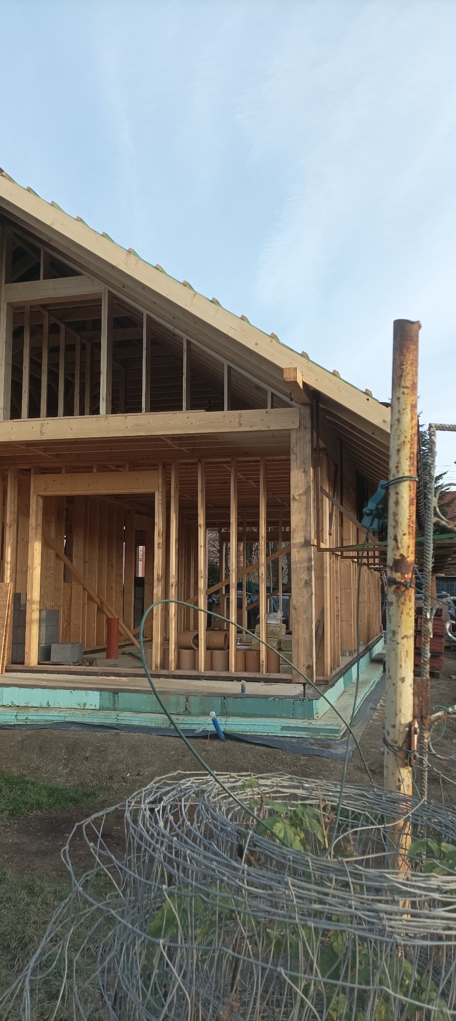 Konstrukcja domu szkieletowego w trakcie budowy, widoczne drewniane ramy i więźba dachowa, z bliska, z elementami rusztowania i materiałów budowlanych w tle.