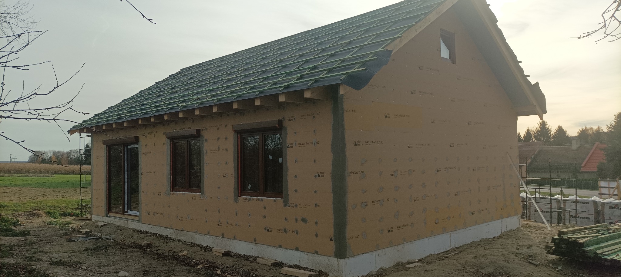 Surowy stan domu szkieletowego z widoczną więźbą dachową w Goli Dzierżoniowskiej. Budynek w trakcie budowy, z oknami i przygotowaną konstrukcją dachu.