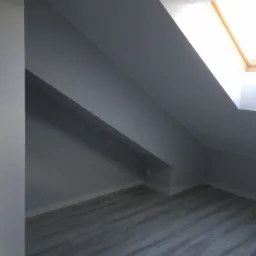 Pomalowane na szaro poddasze z drewnianą podłogą i oknem dachowym wpuszczającym jasne światło.