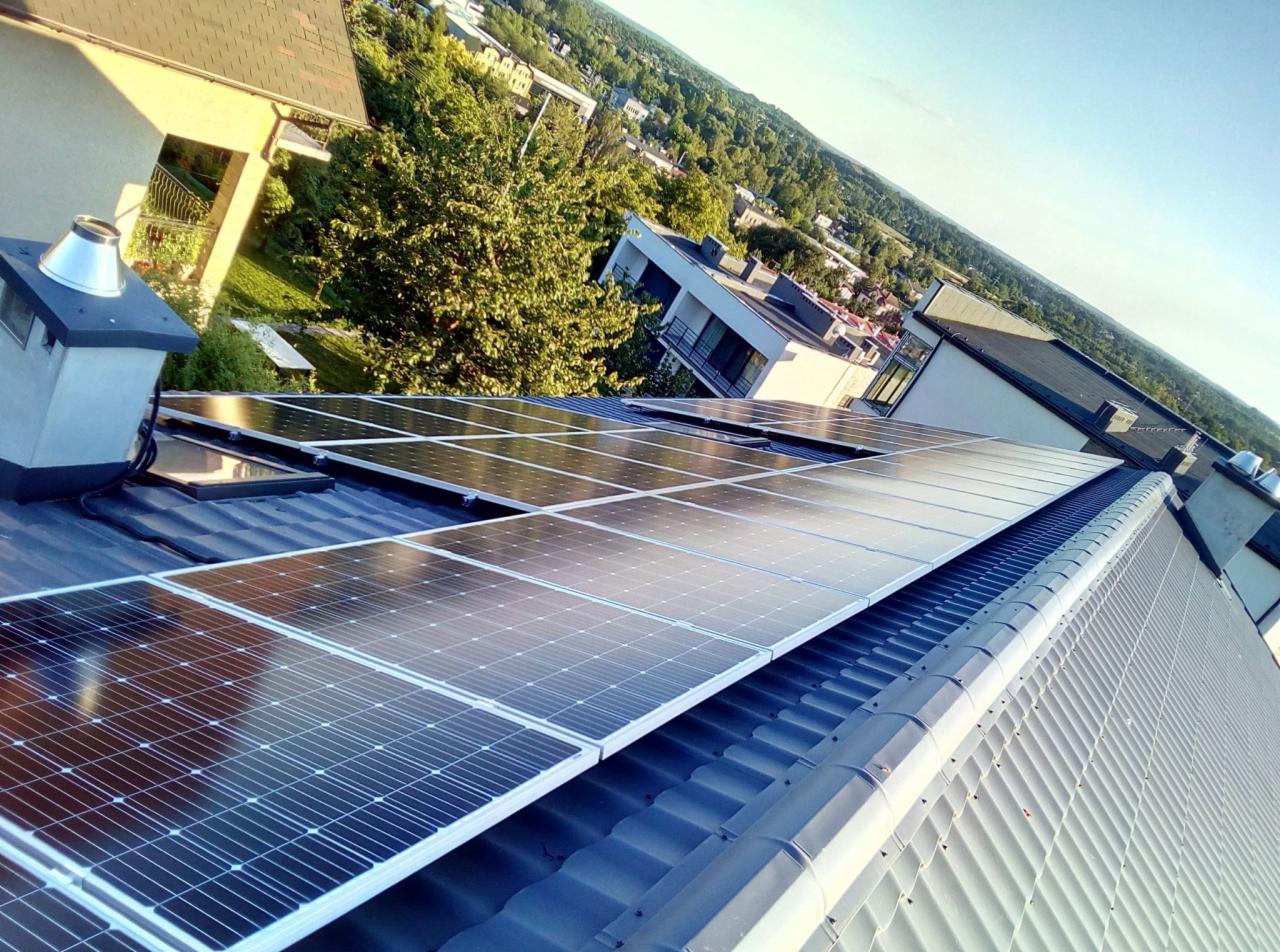 Instalacja paneli fotowoltaicznych na dachu domu w Bielsku-Białej, widok z góry na panele odbijające niebo, w tle zabudowa miejska i zieleń.