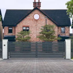 Nowoczesna, pozioma brama przesuwna z szarych paneli metalowych, zamontowana na białych, murowanych słupkach, z widoczną nazwą firmy Horizon Super Wide na jednym ze słupków.