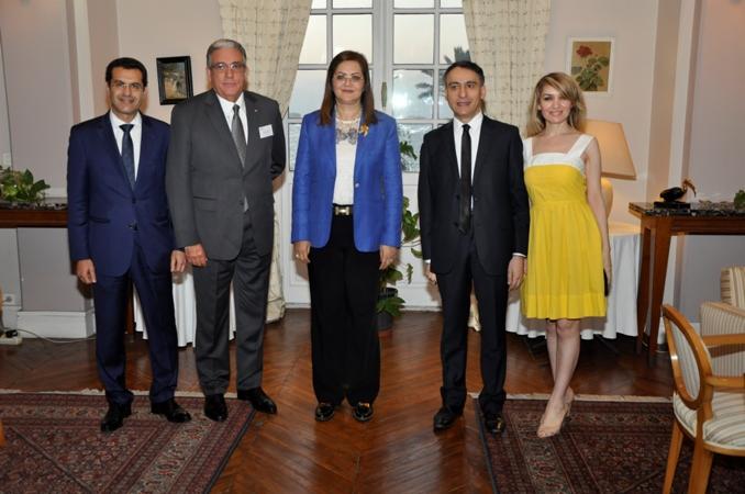 Grupa elegancko ubranych osób pozuje do zdjęcia w Paryżu, w tle widoczne okno z zasłonami i obraz na ścianie.