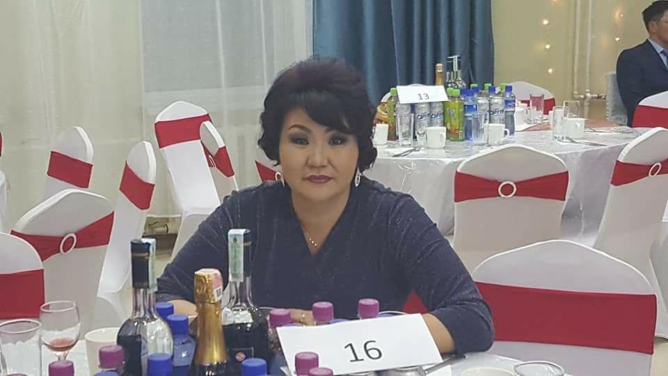 Kobieta siedząca przy stole bankietowym z numerem 16, otoczonym butelkami napojów i win, w tle białe krzesła z czerwonymi wstążkami.