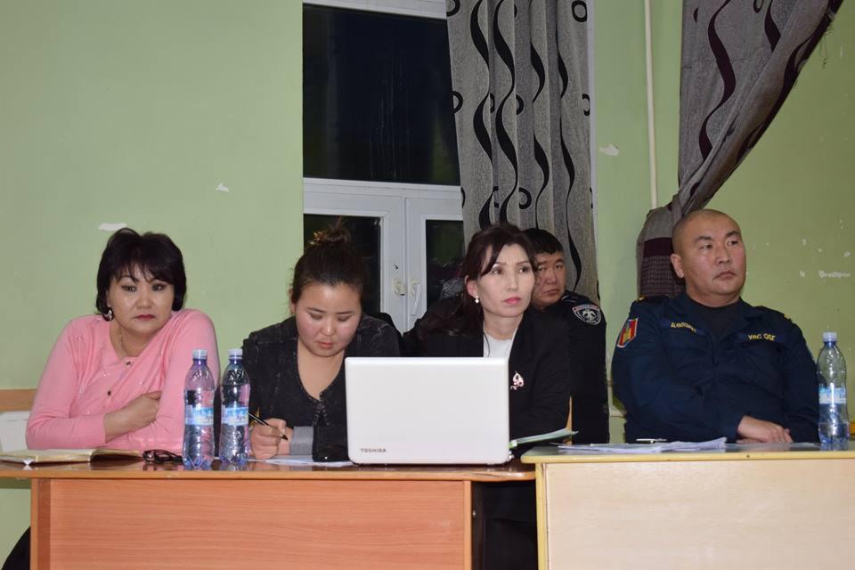 Cztery osoby przy stole podczas spotkania, jedna z nich używa laptopa Toshiba, pozostałe robią notatki, w tle okno z zasłonami.