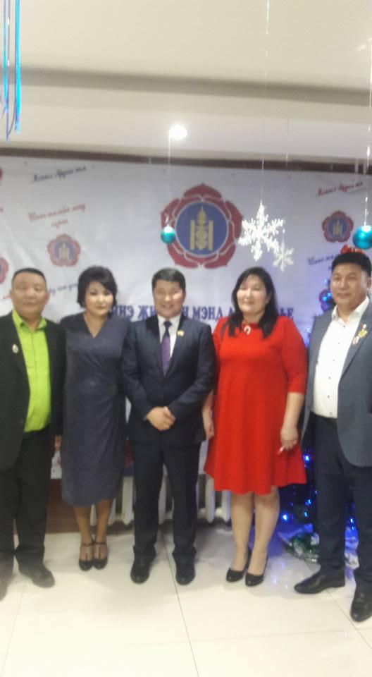 Grupa pięciu osób pozuje na tle dekoracji z motywami flagi Mongolii i śnieżynek, prawdopodobnie podczas wydarzenia firmowego lub uroczystości.