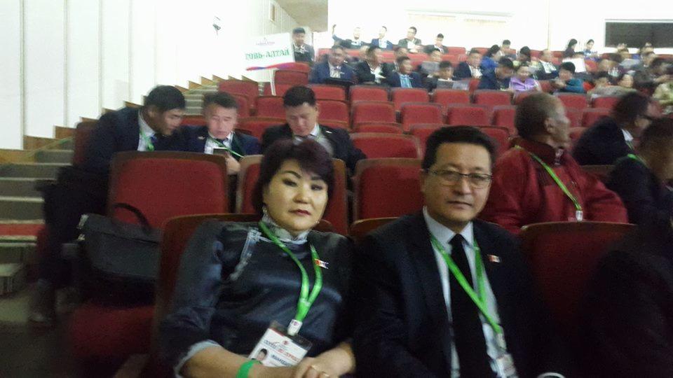 Sala konferencyjna wypełniona uczestnikami, w pierwszym rzędzie kobieta i mężczyzna z identyfikatorami na szyjach, uśmiechający się do kamery.