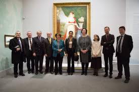 Grupa osób w eleganckich strojach stoi przed obrazem w muzeum lub galerii sztuki, prawdopodobnie podczas wydarzenia biznesowego lub kulturalnego.