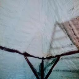 Poddasze z drewnianą konstrukcją pokryte grubą warstwą białej pianki izolacyjnej o nieregularnej fakturze, widoczne fragmenty belek stropowych.