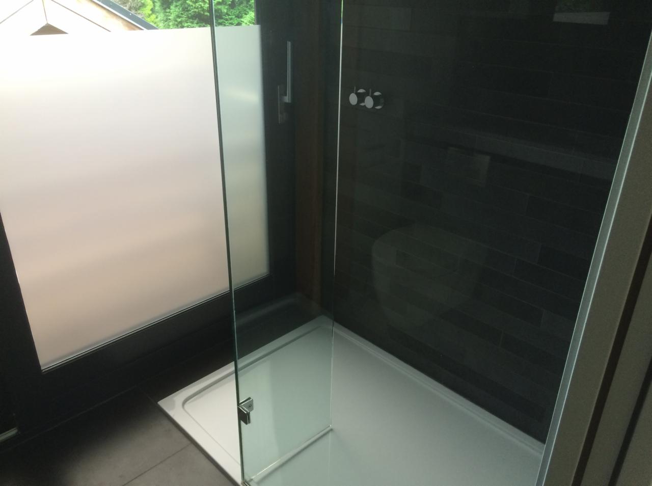 Nowoczesna kabina prysznicowa z czarnymi płytkami ułożonymi poziomo, przeszklone drzwi z chromowanymi zawiasami i matowa szyba w oknie obok.