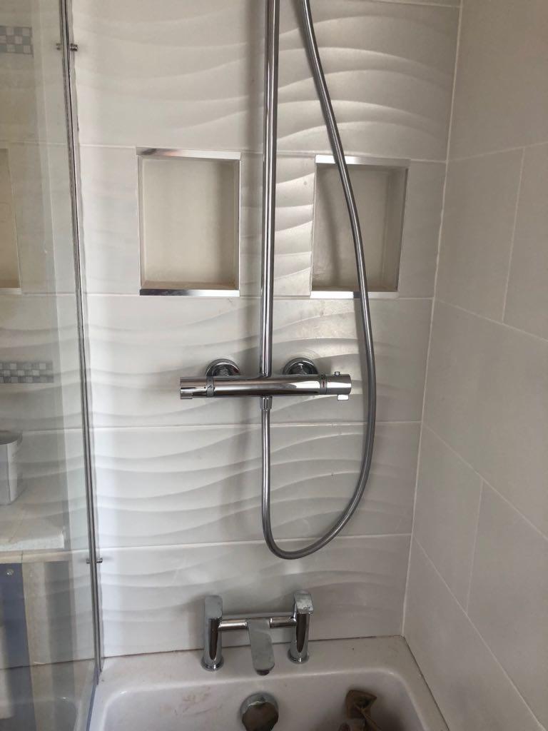 Wykończona łazienka z białą wanną, chromowaną armaturą i dekoracyjnymi płytkami ściennymi z wnękami na kosmetyki.