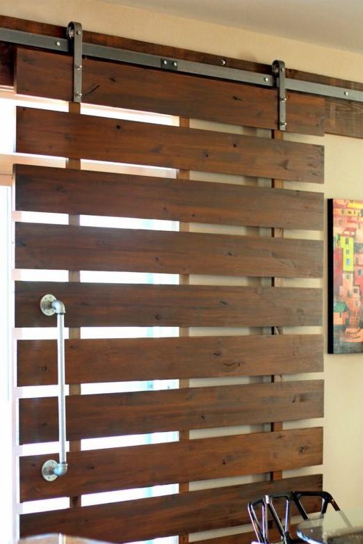 Przesuwne drzwi z ciemnego drewna, poziome deski z przerwami, metalowe okucia i uchwyt z rur, obraz na ścianie w tle.