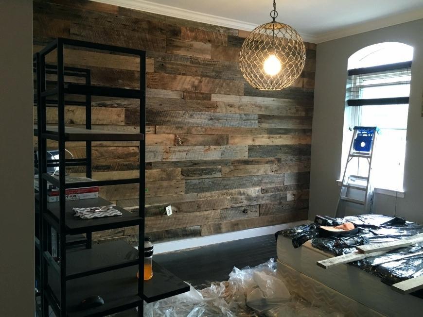 Ściana akcentowa z desek z recyklingu w trakcie montażu, widoczna czarna metalowa półka, lampa wisząca z okrągłym ażurowym kloszem i okno z drabiną, pomieszczenie w trakcie wykończenia.