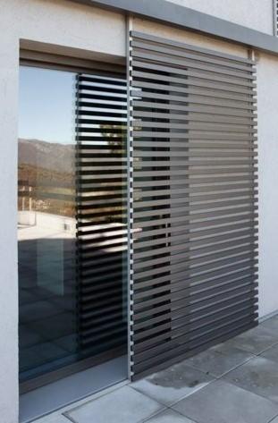 Zewnętrzne żaluzje przesuwne w kolorze szarym, zamontowane przy oknie tarasowym, z widokiem na góry w tle.