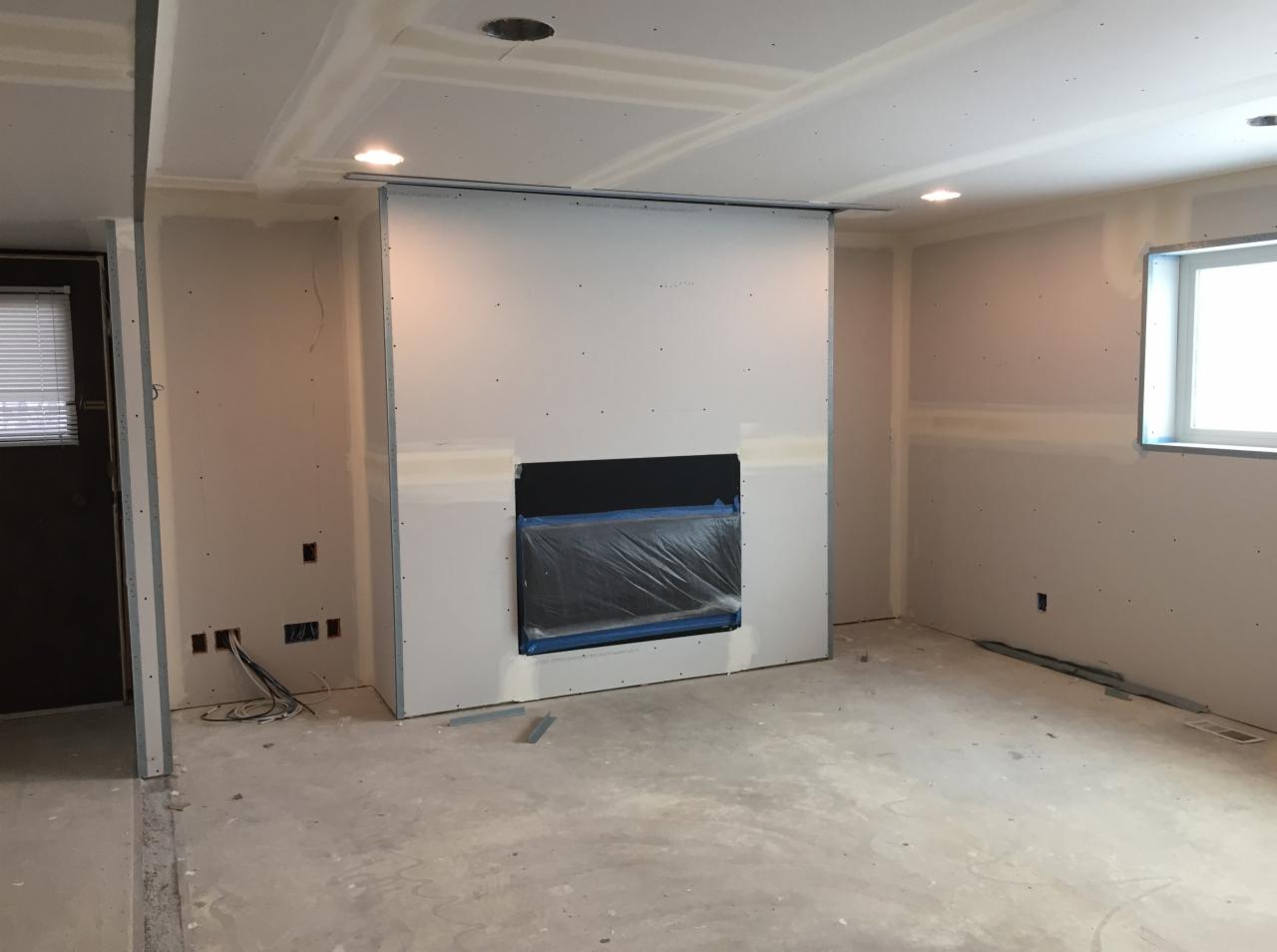 Surowe wnętrze w trakcie remontu: ściany z płyt gipsowo-kartonowych, przygotowane podłoże kominkowe zabezpieczone folią, widoczne przewody elektryczne i otwory na gniazdka, sufit z zamontowanym...