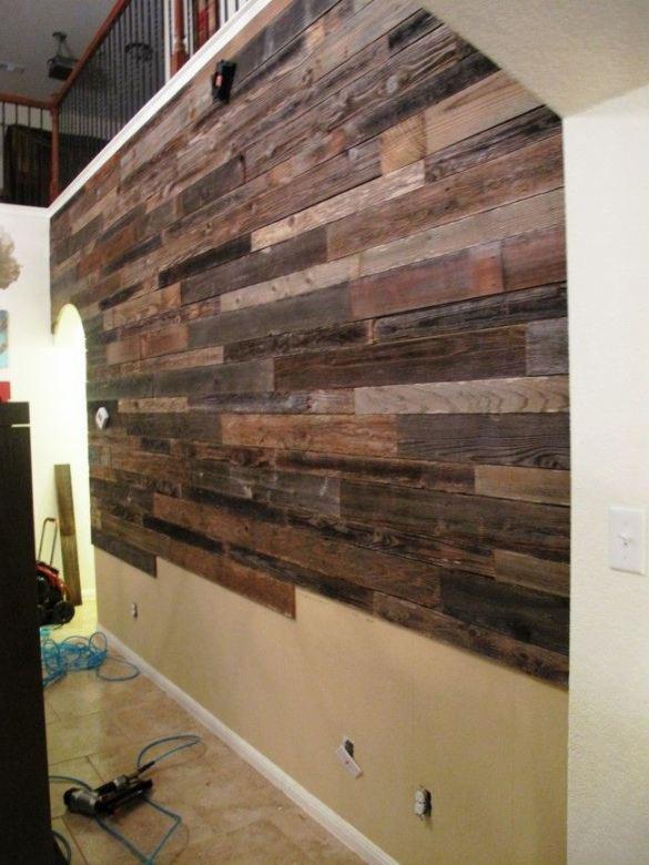 Ściana z desek w trakcie montażu, widoczne narzędzia, nieukończona instalacja elektryczna, surowe drewno i beżowa ściana poniżej.