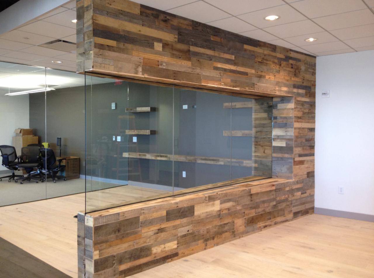 Przeszklona ściana działowa z drewnianą okładziną z desek o zróżnicowanym odcieniu, widok na biuro z półkami i krzesłami, jasna podłoga.