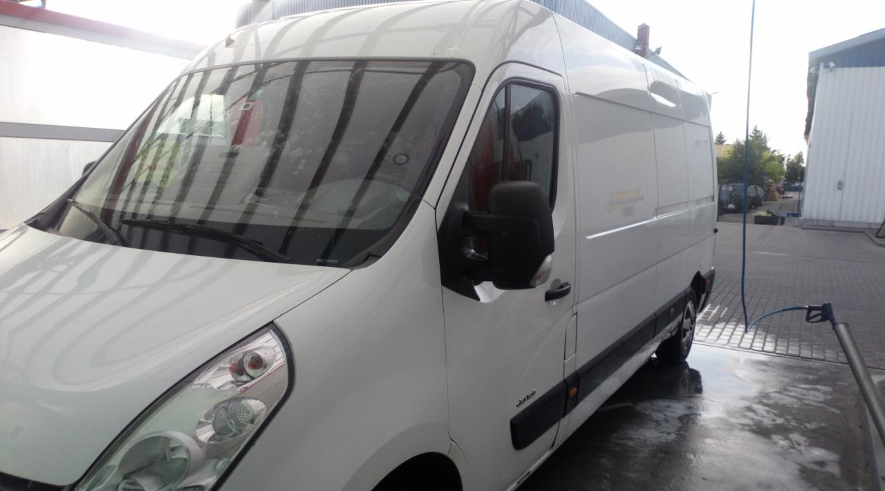 Biały bus dostawczy myty pod ciśnieniem w myjni we Wloclawku, widoczna mokra nawierzchnia i lanca myjąca.