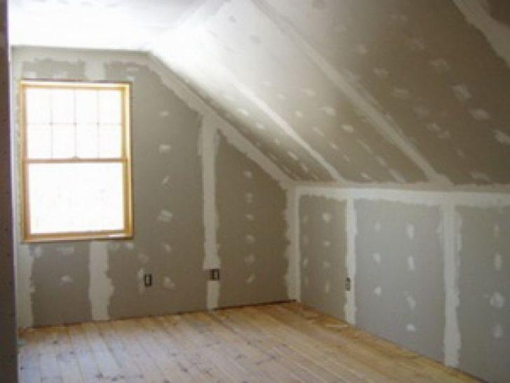 Poddasze w trakcie wykańczania: ściany i skośny sufit z płyt gipsowo-kartonowych, szpachlowane łączenia, surowa drewniana podłoga i okno w drewnianej ramie.