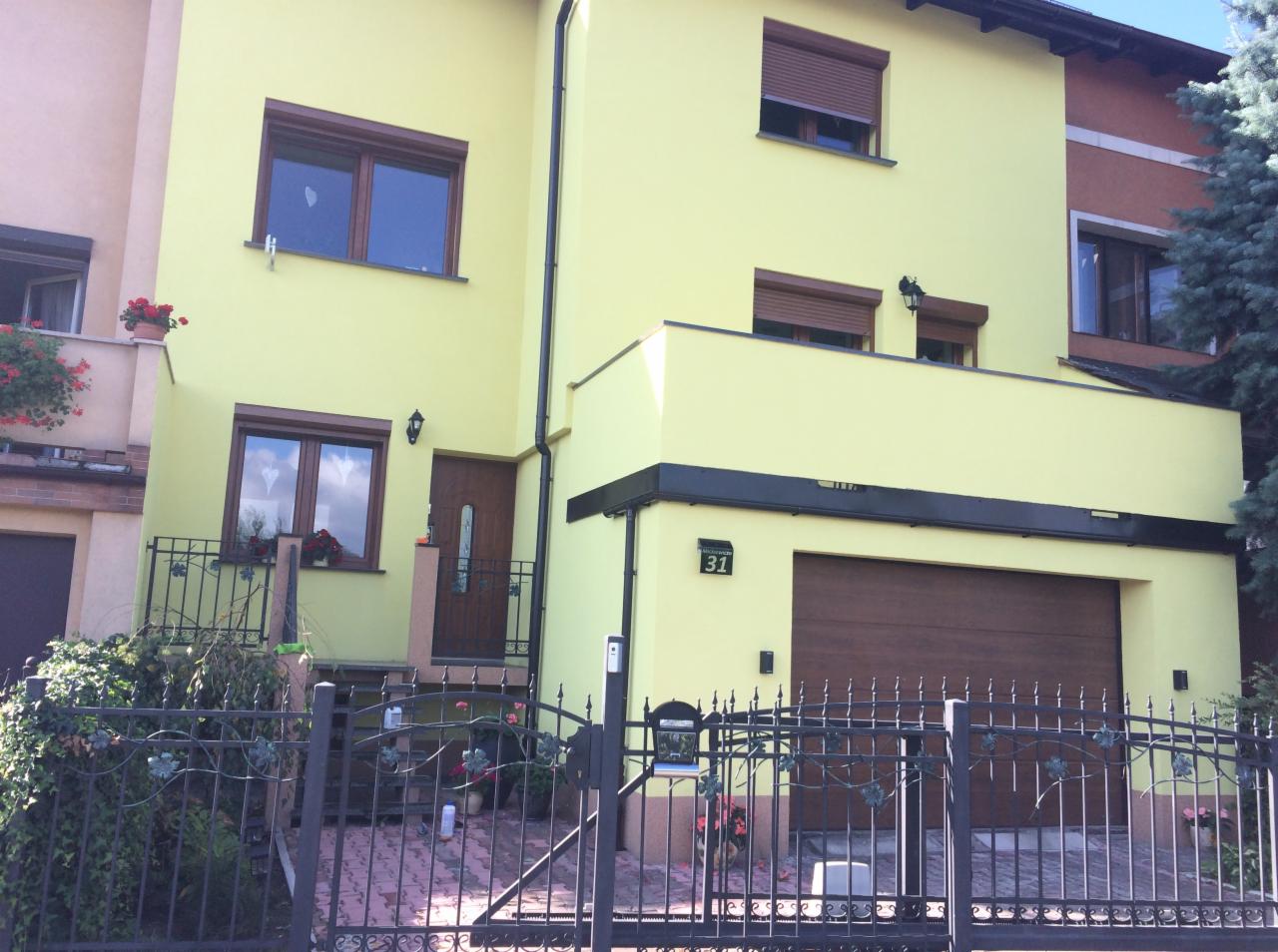 Żółty dom jednorodzinny z brązowymi oknami i roletami, czarnym ogrodzeniem i numerem domu 31.