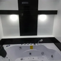 Biała wanna z hydromasażem w nowoczesnej łazience z czarno-białymi płytkami i oświetleniem punktowym.