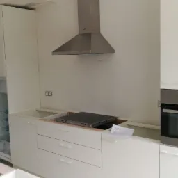 Wnętrze kuchni w trakcie montażu: białe szafki z szufladami, otwarta lodówka, płyta indukcyjna w montażowym otworze i okap nad nią oraz zabudowany piekarnik AEG.