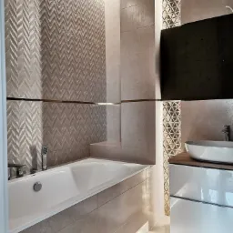 Nowoczesna łazienka z wanną, umywalką nablatową i dekoracyjnymi płytkami z geometrycznym wzorem, podświetlenie LED.