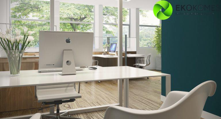 Nowoczesne biuro z białym biurkiem, komputerem Apple, kwiatami w wazonie i widokiem na zieleń za oknem, logo firmy w prawym górnym rogu.