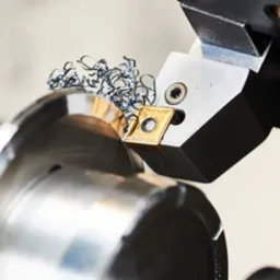 Metalowa obróbka tokarska z widocznymi wiórami i ostrzem noża tokarskiego