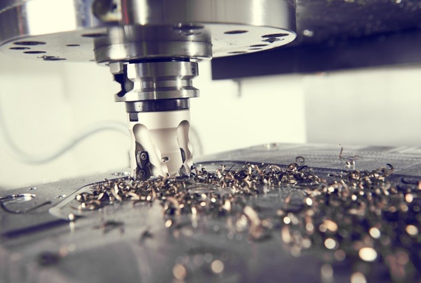 Frezarka CNC w trakcie obróbki metalu, widoczne wióry na powierzchni roboczej.