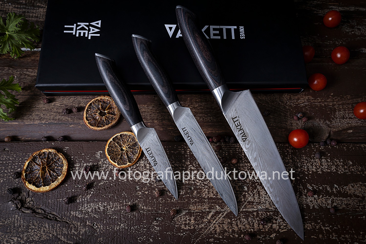 Zestaw trzech noży Valkett z damasceńską stalą, ułożonych na drewnianym stole z suszonymi pomarańczami i pomidorami, prezentowany w studio fotografii produktowej.