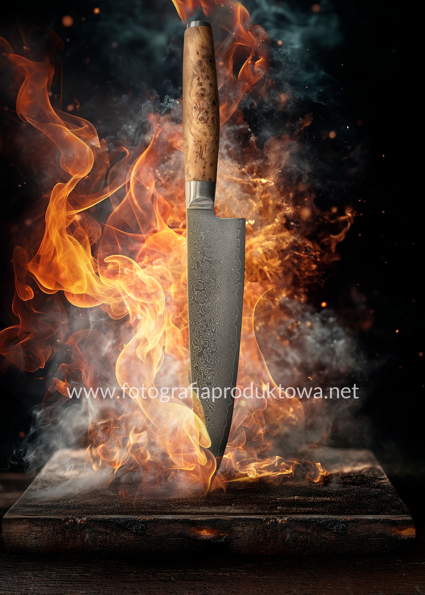 Nóż szefa kuchni z wzorem damasceńskim wbity w deskę, otoczony efektami ognia i dymu, na ciemnym tle. Precyzyjna fotografia produktowa z dbałością o detale.