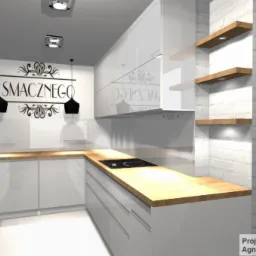 Wizualizacja nowoczesnej, białej kuchni z drewnianym blatem, czarnymi lampami wiszącymi i napisem 'Smacznego' na ścianie, uzupełniona o drewniane półki na tle ściany z białej cegły.