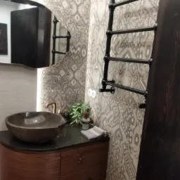 Nowoczesna łazienka z umywalką w kształcie misy, baterią w kolorze miedzi i grzejnikiem drabinkowym na tle ściany w geometryczne wzory.