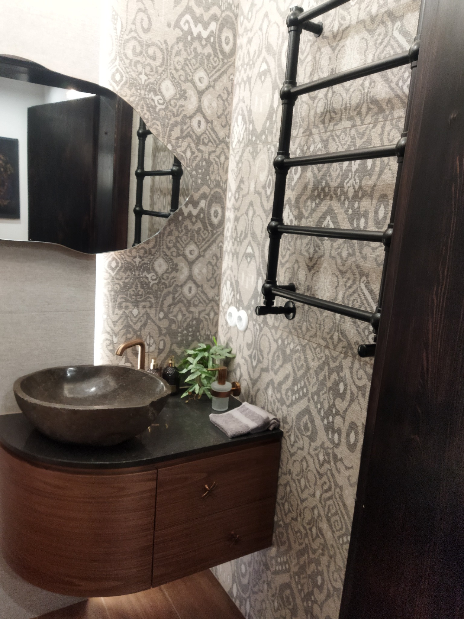 Nowoczesna łazienka z umywalką w kształcie misy, baterią w kolorze miedzi i grzejnikiem drabinkowym na tle ściany w geometryczne wzory.