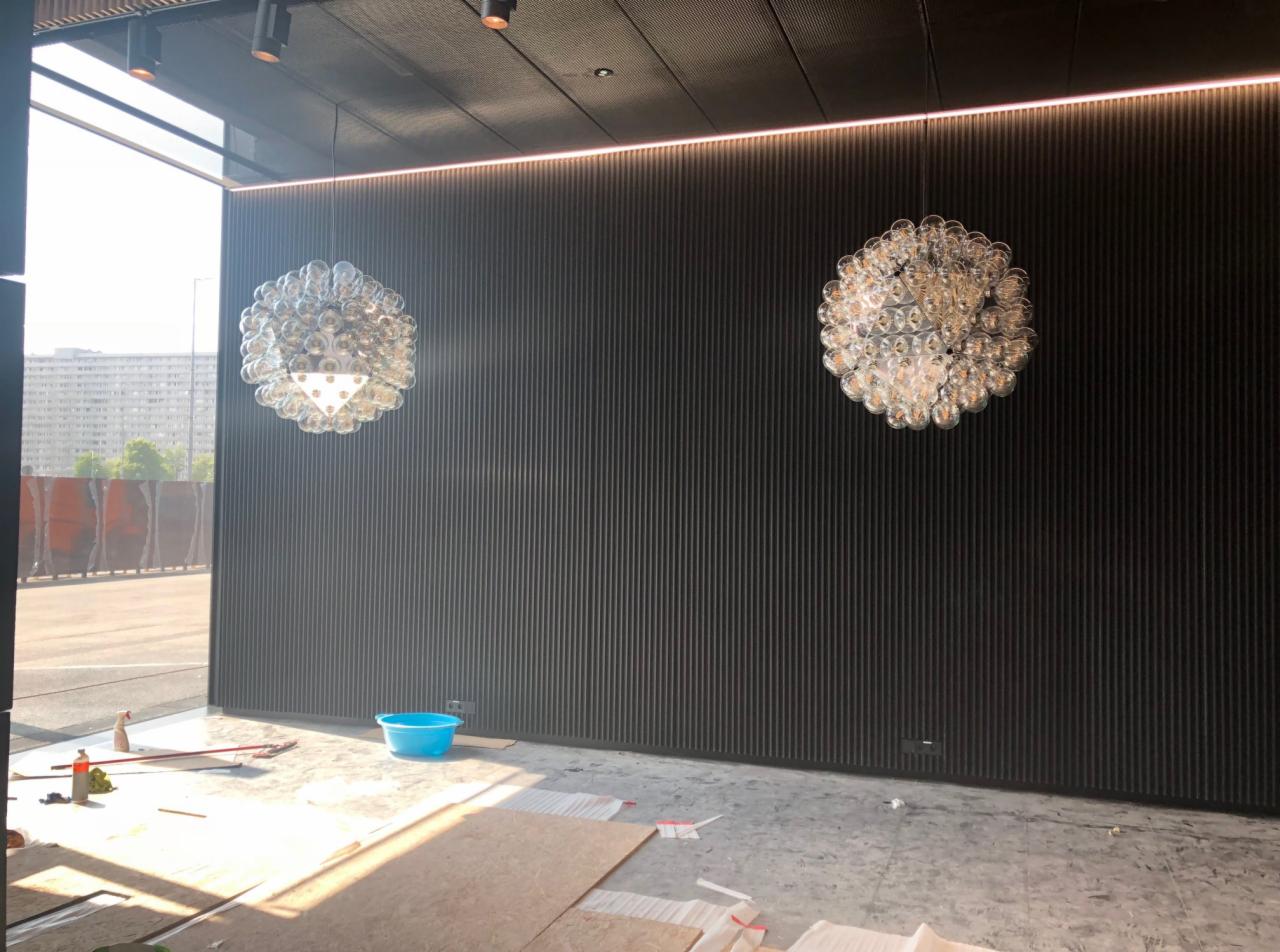 Wnętrze lokalu KTW w trakcie otwierania: widoczne wiszące lampy kuliste, ciemna ściana z pionowymi panelami, podłoga w trakcie wykańczania, niebieska miska i narzędzia.