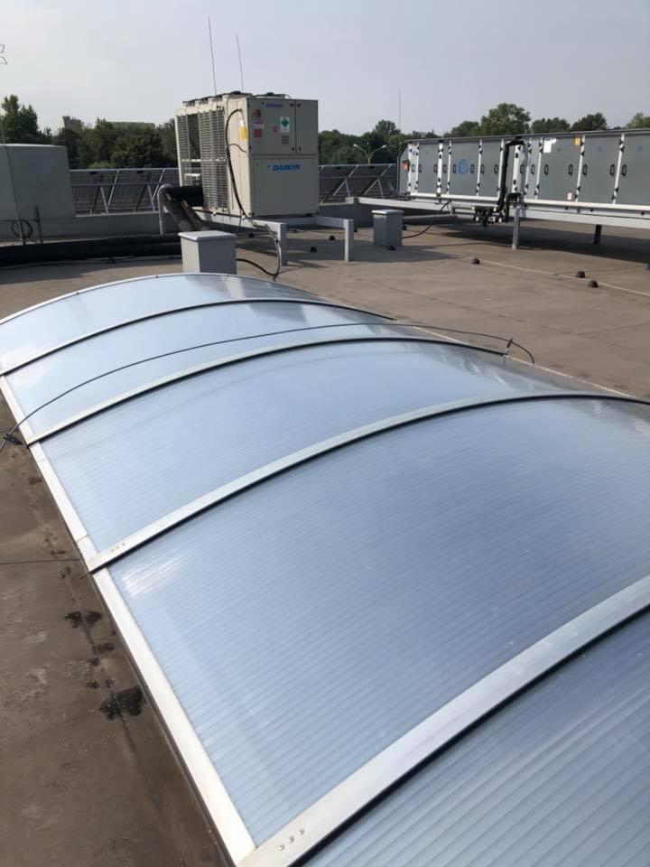 Przezroczyste zadaszenie z poliwęglanu na dachu budynku, w tle klimatyzatory Daikin i inne urządzenia techniczne.