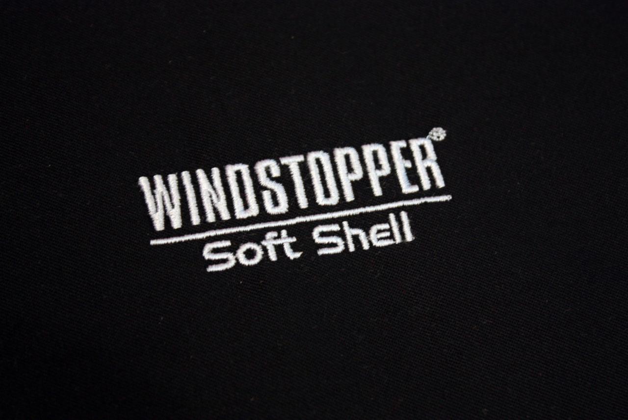 Czarna tkanina z wyhaftowanym białym napisem 'WINDSTOPPER Soft Shell', widoczne detale szwów.