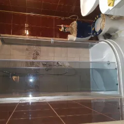 Kabina prysznicowa z przesuwnymi drzwiami w łazience z brązowymi płytkami na ścianach i podłodze, widoczna toaleta z niebieską deską.