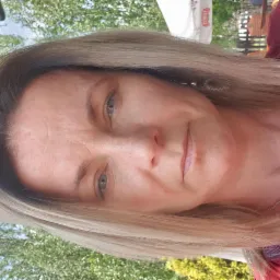 Portret kobiety z blond włosami i srebrną biżuterią, na zewnątrz w słoneczny dzień.