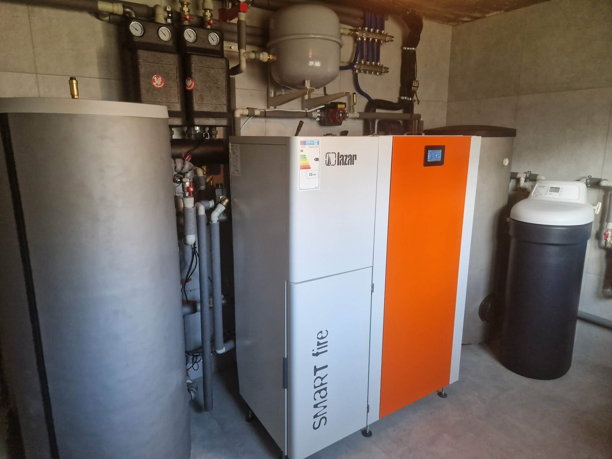 Nowoczesny piec Smart Fire Lazar w kotłowni w Sulmierzycach. Widoczne rury, zbiornik wyrównawczy i filtry. Pomieszczenie wykończone płytkami.
