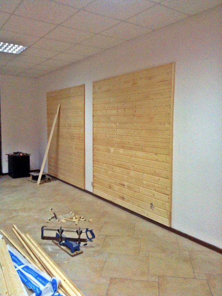 Montaż drewnianej boazerii ściennej: widoczne deski, narzędzia stolarskie, wióry i listwy przypodłogowe w trakcie prac wykończeniowych.