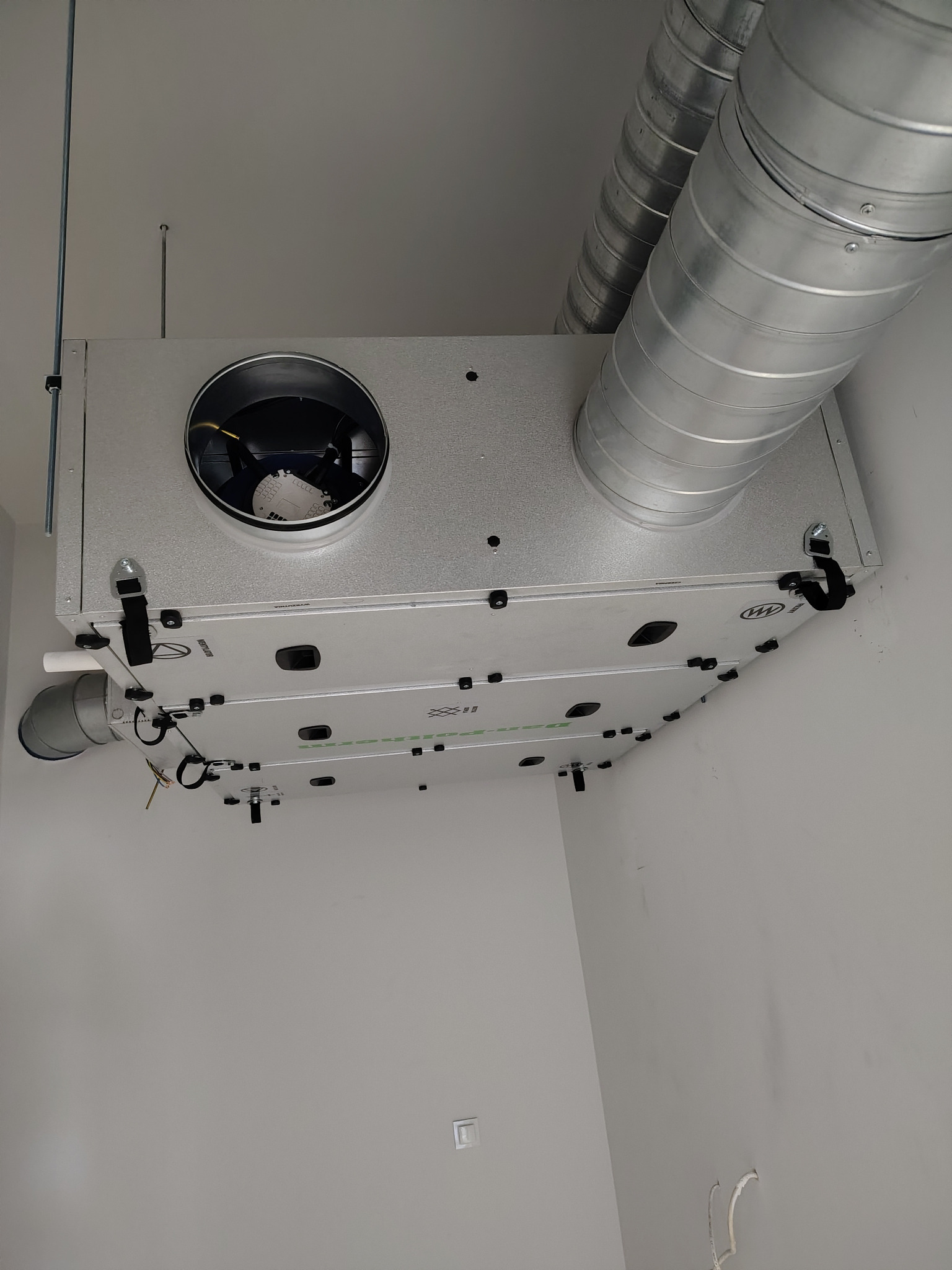 Zamontowany rekuperator z widocznymi przewodami wentylacyjnymi w Ornecie. Srebrny rekuperator podwieszony pod sufitem w jasnym pomieszczeniu.