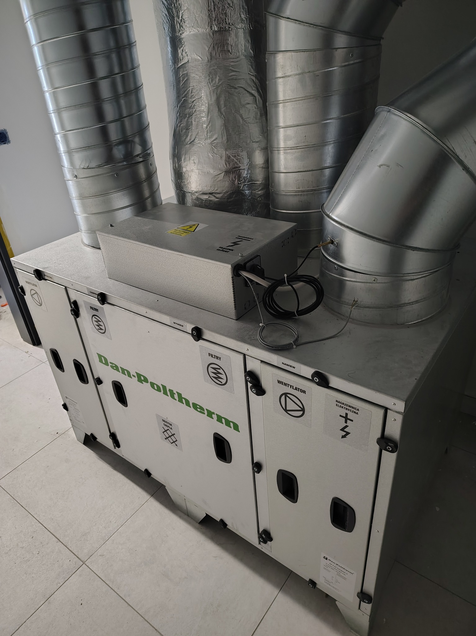 Zmontowana jednostka rekuperacyjna Dan-Poltherm z podłączonymi przewodami wentylacyjnymi, widok z perspektywy, na jasnej podłodze z płytek.