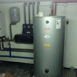 Piwnica z zamontowanym piecem gazowym Vaillant, zbiornikiem na wodę Termica Inoxsolar oraz instalacją hydrauliczną z niebieskimi rurami.