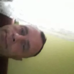 Portret mężczyzny z bliska, z widocznym fragmentem sufitu i ściany w tle, z nietypowym kątem ujęcia.