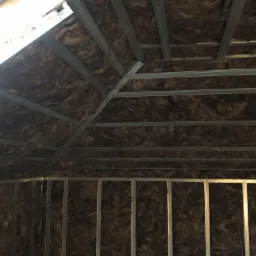 Ocieplenie poddasza wełną mineralną, widoczne metalowe profile konstrukcyjne, etap prac wykończeniowych.