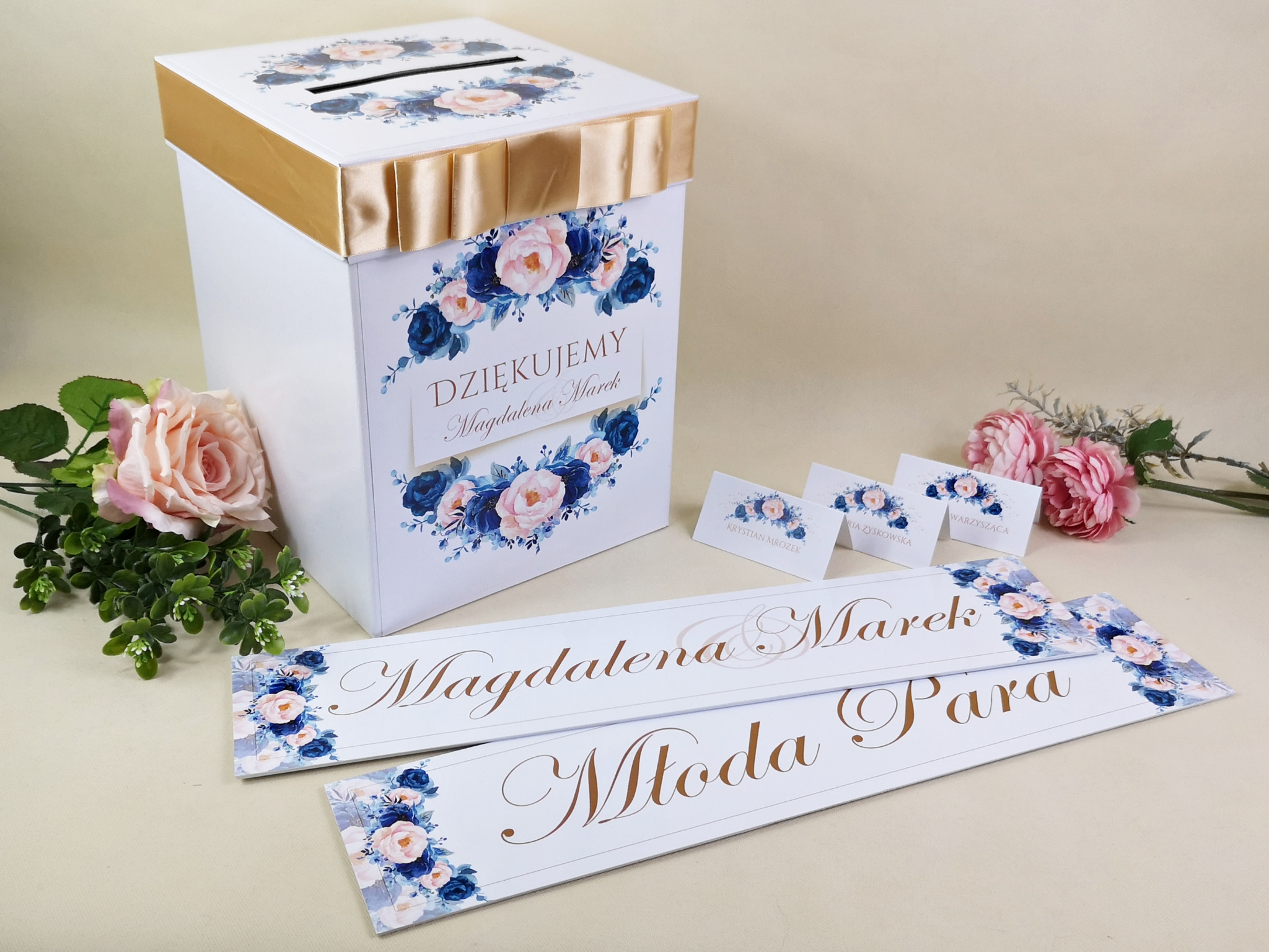 Biała, kwadratowa skrzynka na koperty ślubne z dekoracją kwiatową i złotą wstążką, dopasowane winietki i zawieszki na alkohol, całość w pastelowej kolorystyce.