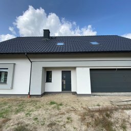 FENESTRA - Nowoczesny dom jednorodzinny z grafitową bramą garażową segmentową, drzwiami zewnętrznymi w kolorze antracytu, oknami PCV z ciemnymi ramami i dachem z dachówki ceramicznej w odcieniach szarości...